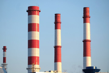 Many high red and white industrial pipes over clear cloudless blue sky on sunny day front view