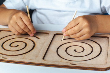 Fototapeta na wymiar Children's montessori wooden toy. Board for interhemispheric development of the brain. Children's hands close-up. Child development retardation. Spiral circle circle 