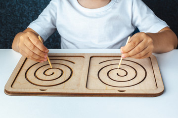 Fototapeta na wymiar Montesori wooden game for the development of children. Child draws on a stencil. Children's wooden toy. Board for interhemispheric development of the brain. Children's hands close-up