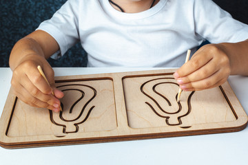 Children's  montessori wooden toy. Board for interhemispheric development of the brain. Children's hands close-up. Child development retardation. Spiral circle circle 