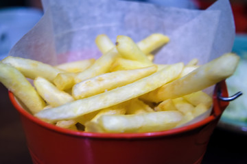 Close-up french fries in a metal bucket on a table in a cafe.