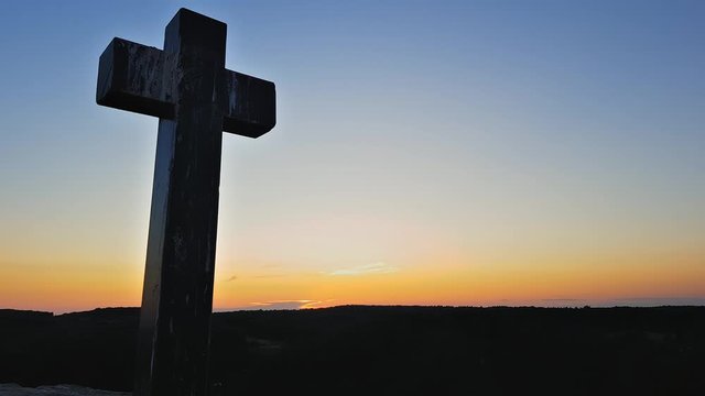 Stone cross on top of a mountain against a sunset. Cross on a sunset background. Stone crem on the mountain at sunset