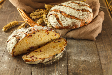 Fresh sliced bread on a dark wooden background with whole bread and wheat in the background