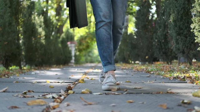 Attractive young business woman with a briefcase in a black jacket and glasses steps, walks and dances outdoors. Rejoices, laughs and has fun in the park. Closeup feet and face. Dancing in park.