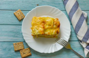 Portion of tasty lasagna on white plate on blue wooden table, blue and white striped towel. homemade food