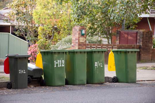Australian garbage wheelie bins with colourful lids for recycling and general household waste lined up on the street kerbside for council rubbish collection