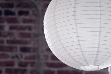 A thin flammable decorative white paper asian oriental style hanging CFL LED light bulb lantern in portrait orientation against interior brick wall