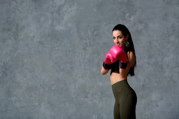 Beautiful athletic girl posing in pink boxing gloves on a gray background. Copy space. Concept sport, fight, goal achievement.