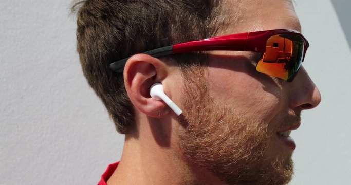Young man wearing wireless earphones going running wearing sport sunglasses for fitness run outdoors. Active person wearing earbuds for exercise. Man listening to audiobook or podcast.