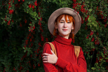 Portrait of a young attractive girl with red hair in a hat and a red sweater against the background...