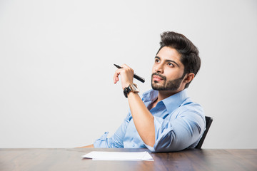 Indian businessman writing a document while sitting at desk or work station