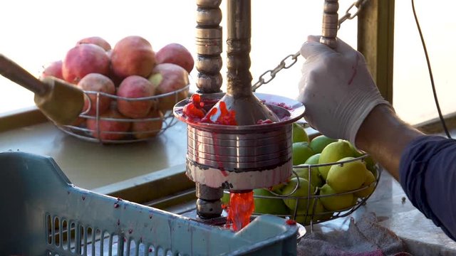 Pomegranate being squeezed in a juicer press with juice splashing out in slow motion