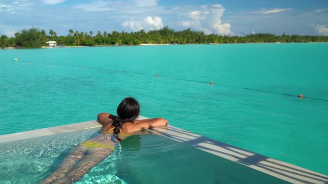 Seamless Loop video: Sexy bikini body woman relaxing swimming in luxury infinity pool of resort hotel lying in water floating in yellow bikini. Tanned slim body. Looping 4K video.