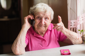 An elderly woman talks on a mobile phone sitting at his home.