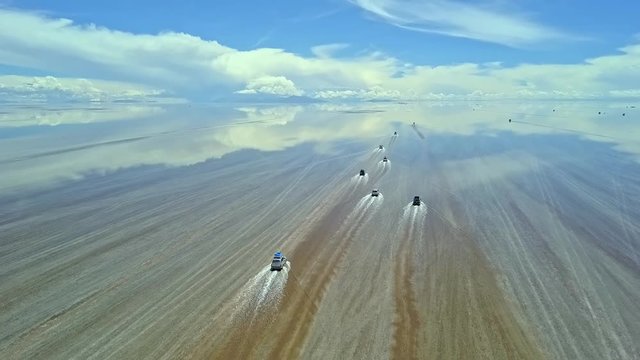 Aerial of four wheel drive vehicles cross the flooded Salar de Uyuni, world's largest salt flat, near Daniel Campos Province, Bolivia. Drone slow tracking shot