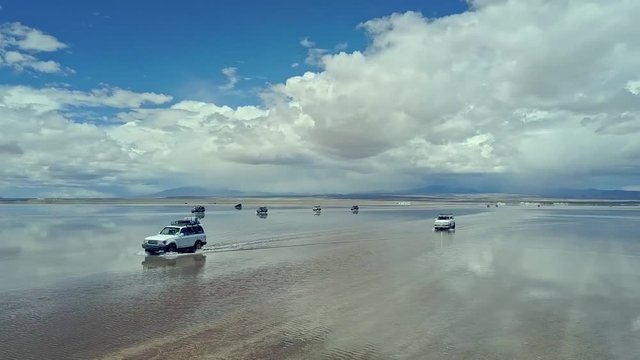 Aerial of four wheel drive vehicles cross the flooded Salar de Uyuni, world's largest salt flat, near Daniel Campos Province, Bolivia. Drone fast left to right pan