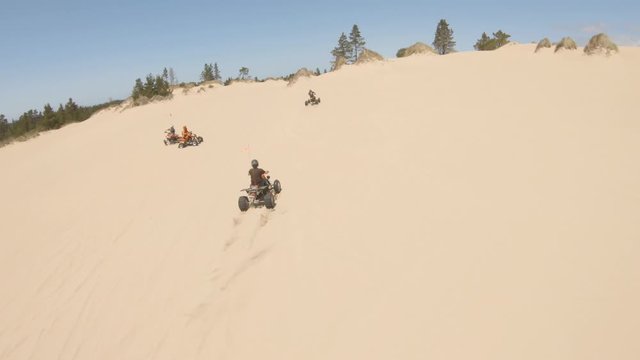 A team of all terrain vehicles blaze across the dunes and one in particular powers ahead of the rest and executes an aggressive doughnut.