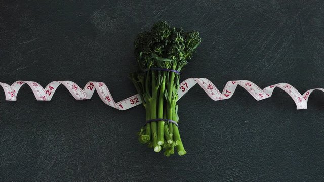 hand placing broccolini on top of measuring tape