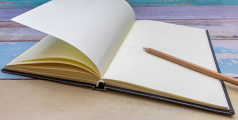 Brown wooden pencil on a notebook placed on an old wooden desk in pastel colors and a black background