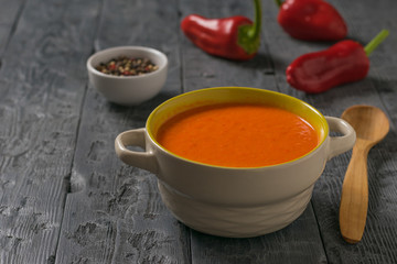 Soup mashed red bell pepper with a wooden spoon on the table.
