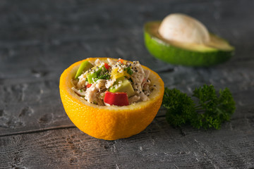 Half orange with chicken and avocado salad on the background of half avocado.