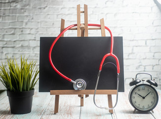 Stethoscope, alarm clock and black board, on wooden background. Healthcare time concept