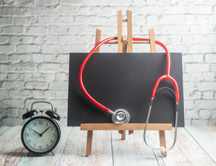 Stethoscope, alarm clock and black board, on wooden background. Healthcare time concept