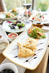 Latin American fried empanadas with Vegetable salad with arugula. Variety of dishes on the table. Various snacks and antipasti on the table. Restaurant menu. Italian cuisine