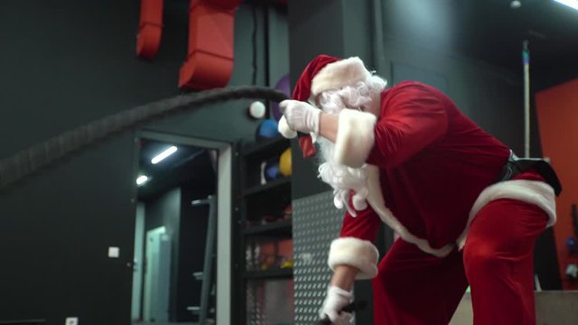 Santa Claus training at the gym on Christmas Day. Santa Claus with battle rope in functional training fitness gym