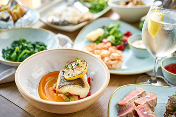 Roasted pike perch or cod fish with baked vegetables. Variety of dishes on the table. . Restaurant...