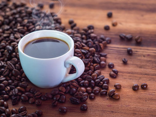 Cup of smoking aromatic coffee and beans on brown table, close up view. Texture of wooden table. Art composition. Selective soft focus. Blurred background