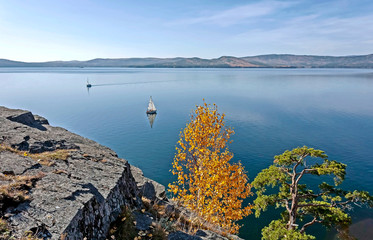 sailing boat on the calm lake Turgoyak, view from the rocky shore in autumn