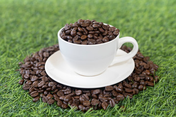 coffee beans in white coffee mugs on the green grass background.
