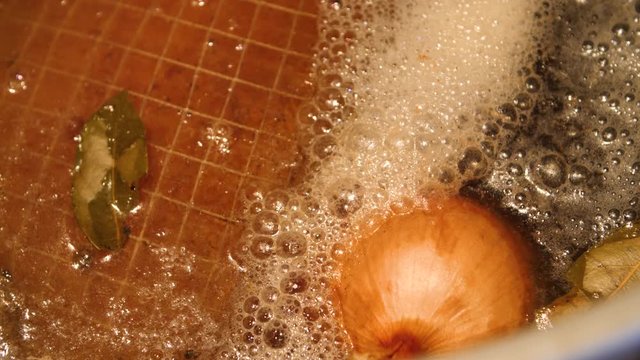 Boil-in-the-bag ham boiling in water with bay leaf and yellow onion in a cooking pot for Easter