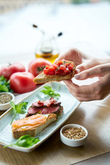 Woman hold in hands Bruschetta with tomatoes. Variety of dishes on the table. Italian cuisine