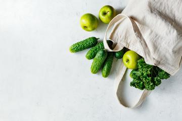 Cotton eco bag with green vegetables on a light background, copy space. Ingredients for healthy food. Top view, copy space.