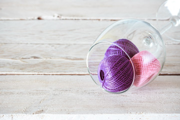Eco-friendly cotton yarn. Skeins of thread in a glass wine glass on a light wooden table. Items for...
