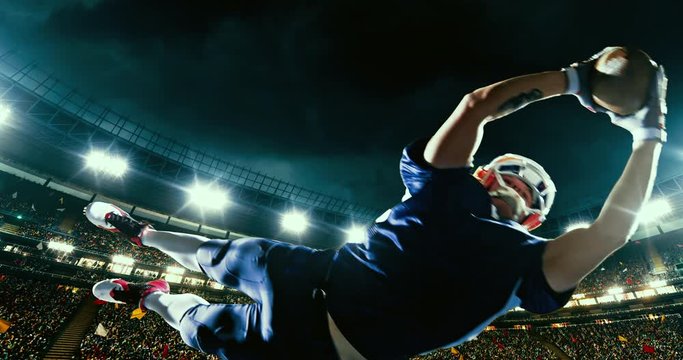 American football player jumps with a ball on a professional sports arena with bleaches full of people. Arena and people on it are made in 3D.