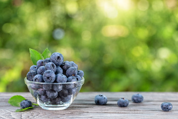 Blueberries in glass bowl and scattered on wooden table