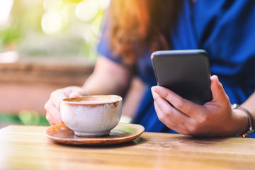 Closeup image of a woman holding and using mobile phone while drinking coffee in the garden