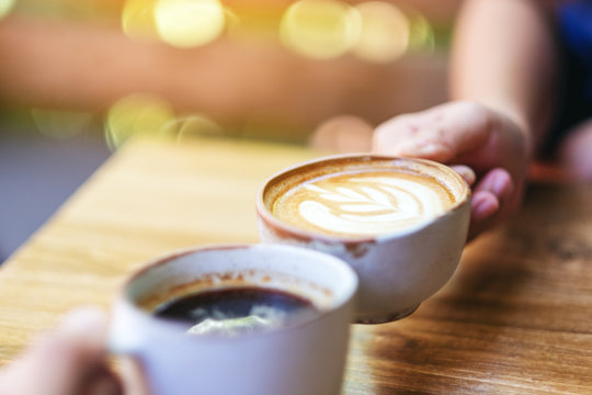 Close up image of two people clinking coffee mugs on wooden table