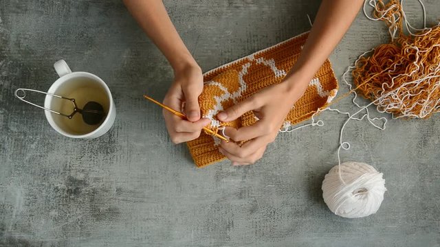 young womans hands crochet hook with orange and white cotton threads on stone tabletop background, view from above close-up full HD stock video footage in realtime