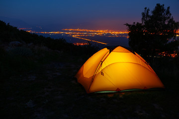 Orange lighted inside tent on mountain above city in night lights