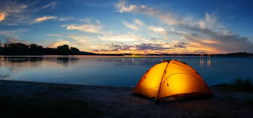  Oranje toeristische verlichte tent aan het meer bij zonsondergang © alexlukin