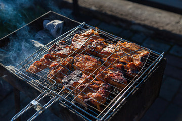 Close-up on the process of cooking shashlik of pork or beef meat clamped in a grill with a crispy burnt crust over gray burnt coals on an open fire with smoke going up.