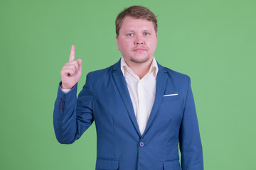 Portrait of handsome overweight bearded businessman pointing up