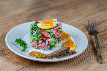 Delicious salad with broccoli, tomato, onion and boiled egg with cream sauce in plate on wooden background. Healthy food