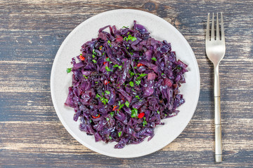 Fried blue cabbage with onion, apple and garlic in plate on wooden table. Top view, closeup