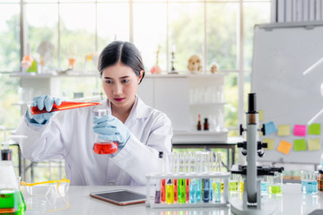 Attractive scientist woman looking chemical sample in flask at laboratory with lab glassware...