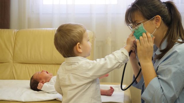 Mother consult newborn baby with stethoscope, big brother take off doctor mask
